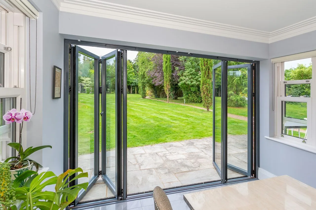 Anthracite-grey framed bifold doors folded open from a bright sitting room onto a landscaped garden
